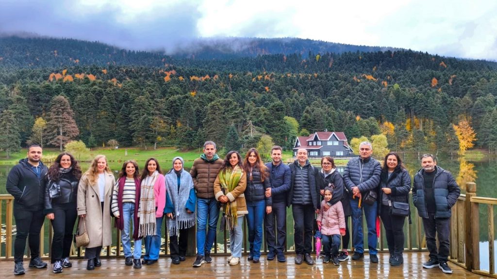 Göl kenarında doğa manzarası eşliğinde kalabalık grup fotoğrafı.