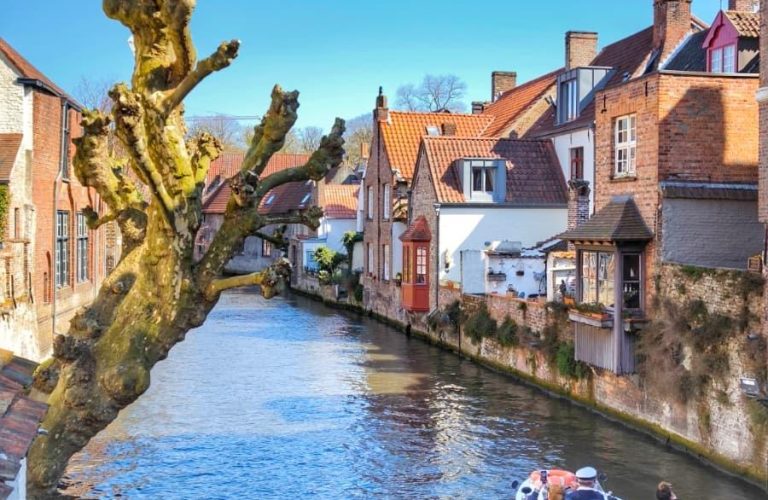 Kanaldan geçen gezi teknesi ve tarihi binalarla çevrili Brugge manzarası.