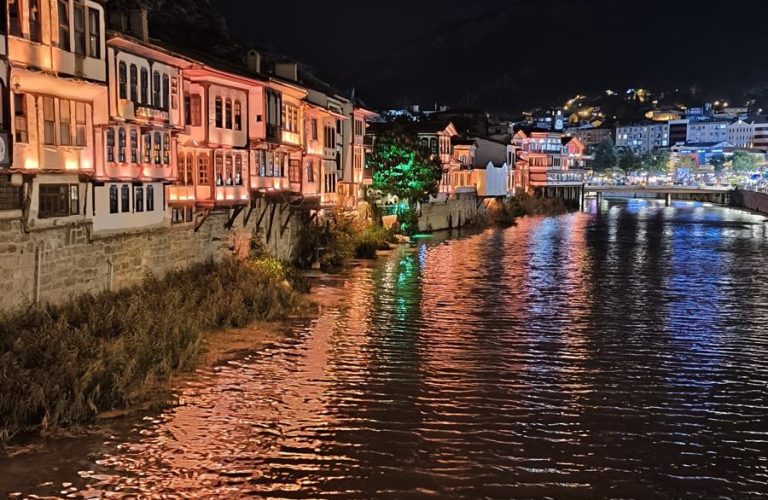 Gece ışıklarıyla aydınlanan tarihi evler ve nehir kıyısı manzarası.