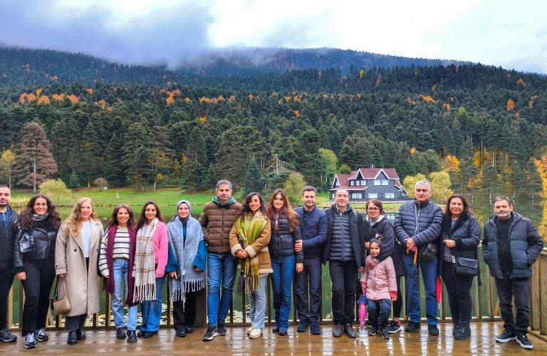 Göl kenarında doğa manzarası eşliğinde kalabalık grup fotoğrafı.