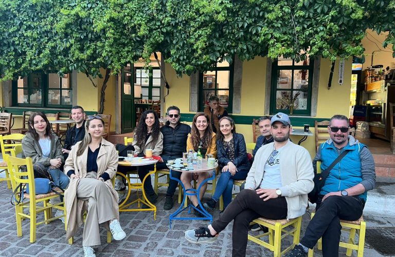 Açık havada kafe masasında oturan kalabalık bir grup insan.