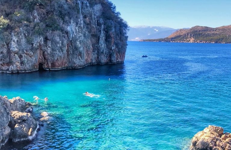 Turkuaz deniz, kayalık koy ve berrak suda yüzen insanlar.